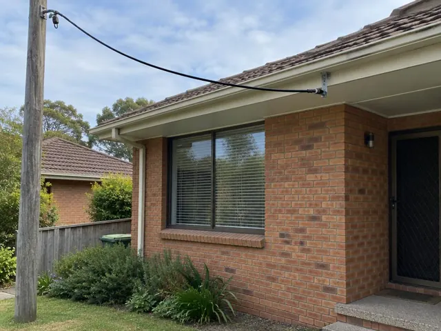 Overhead service cable and point-of-attachment bracket on brick house exterior in Allambie Heights