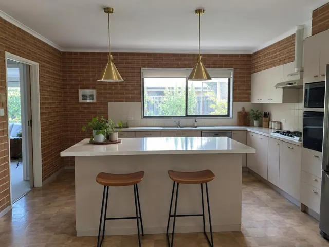 Modern kitchen with two brass pendant lights over an island, brick walls and tiled floor in Beacon Hill